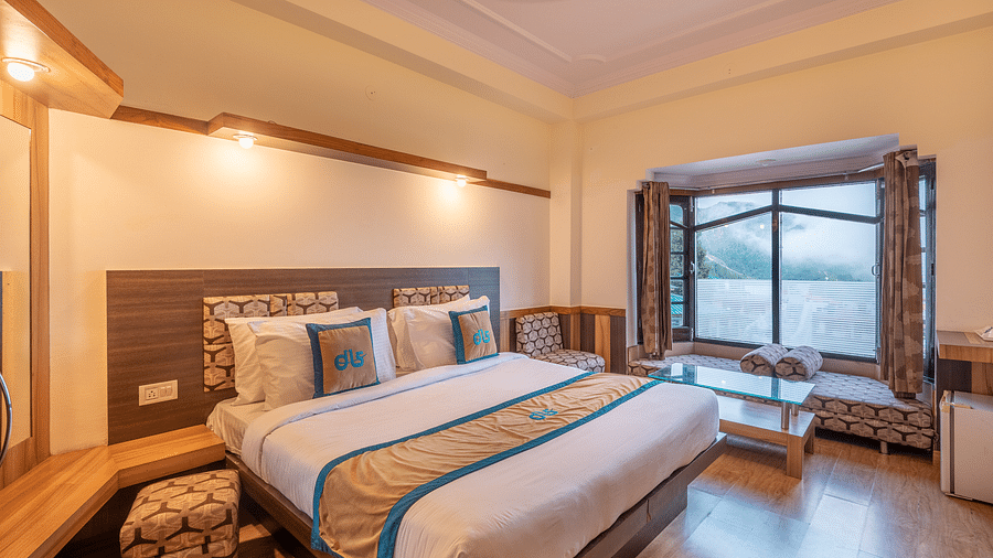A hotel room with a large bed, a window overlooking a mountain view, and a seating area - DLS Meghavan Resort